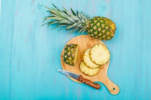 Whole and sliced pineapple in a cutting board with a fruit knife top view on a blue cyan background
